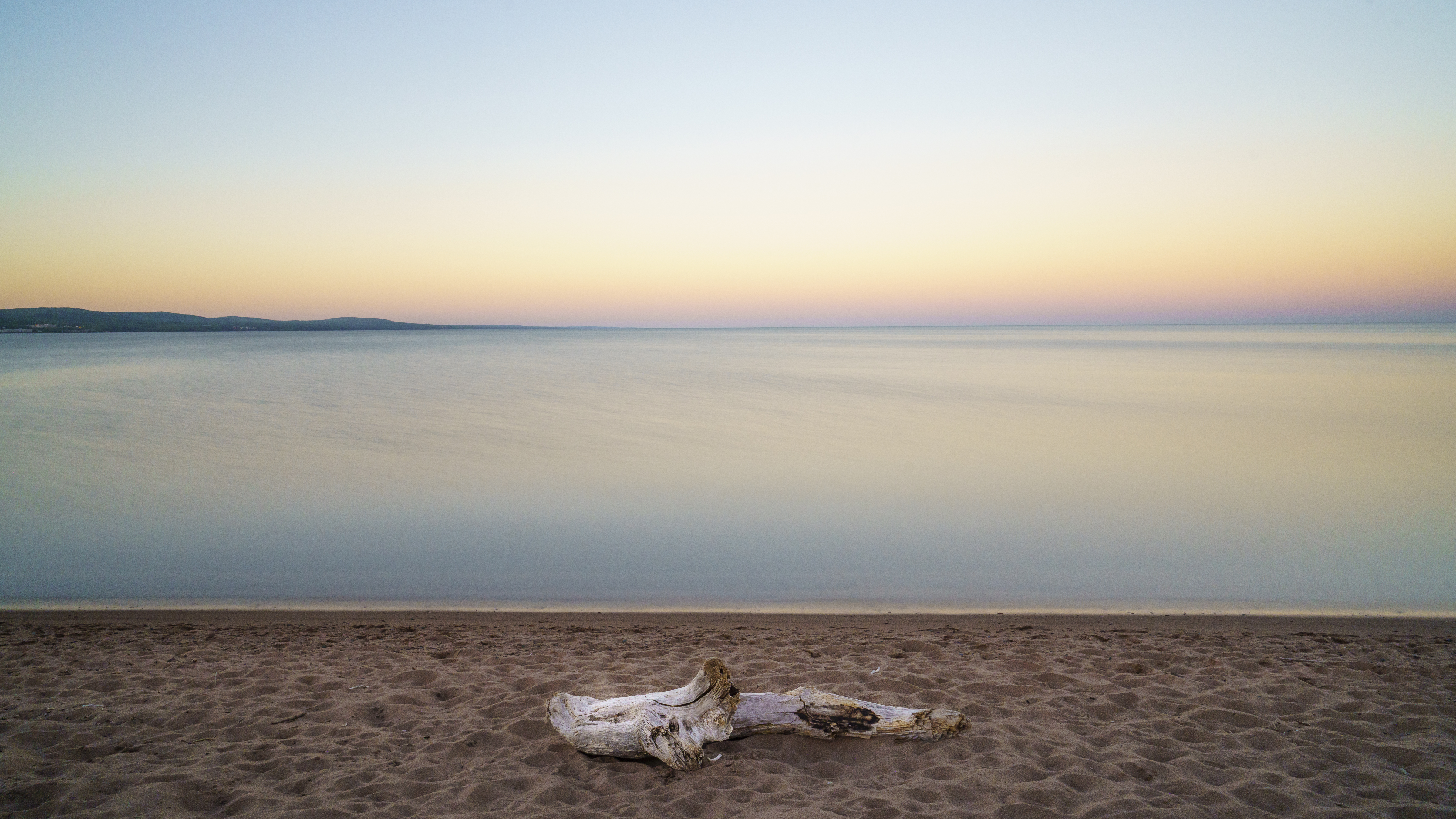 photograph of sandy shore with driftwood looking out onto body of water with a glowing horizon