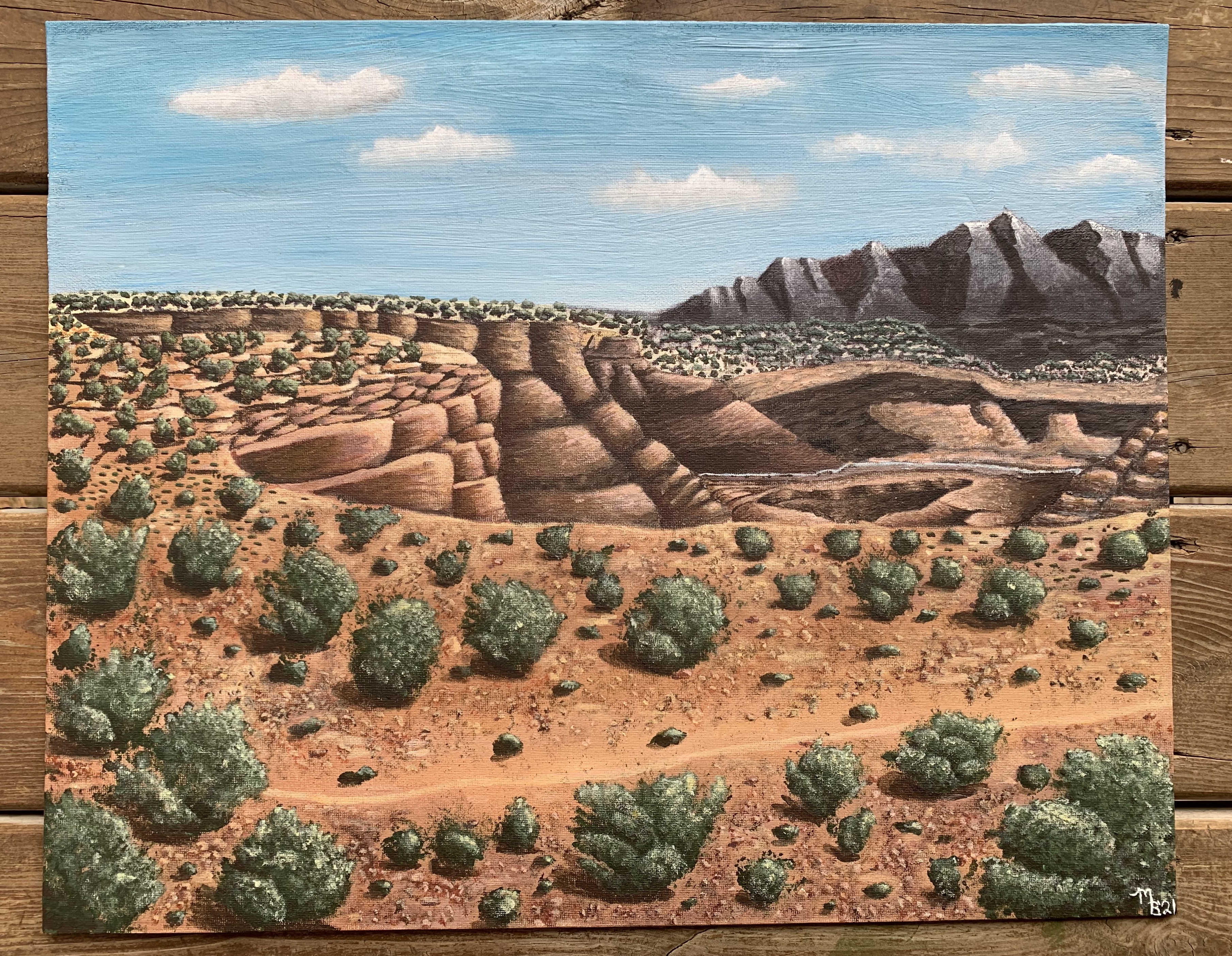 painting of desert landscape with cacti and rocks against a blue sky with clouds