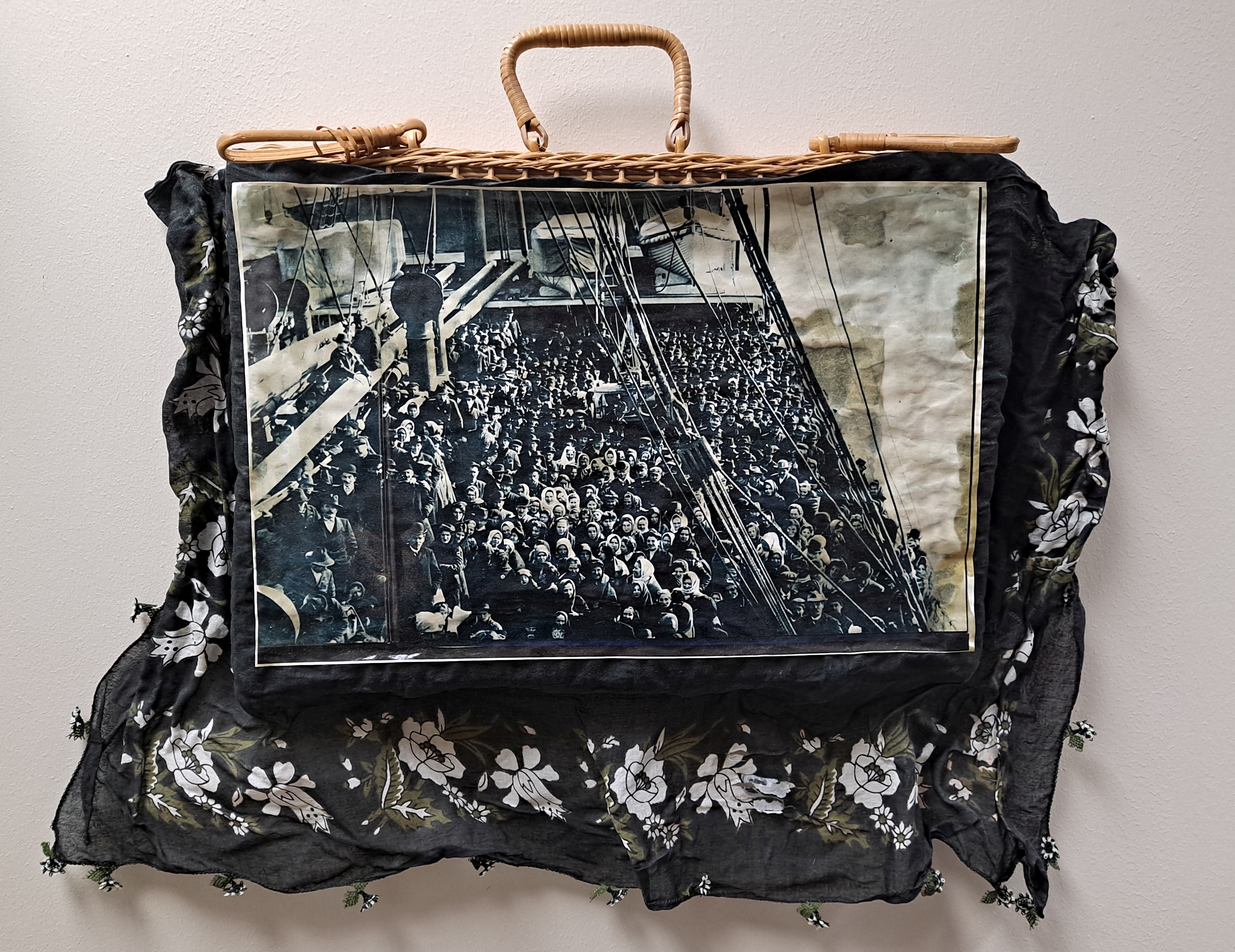 Photograph of wicker suitcase with old photograph of immigrants on it and cloth around it