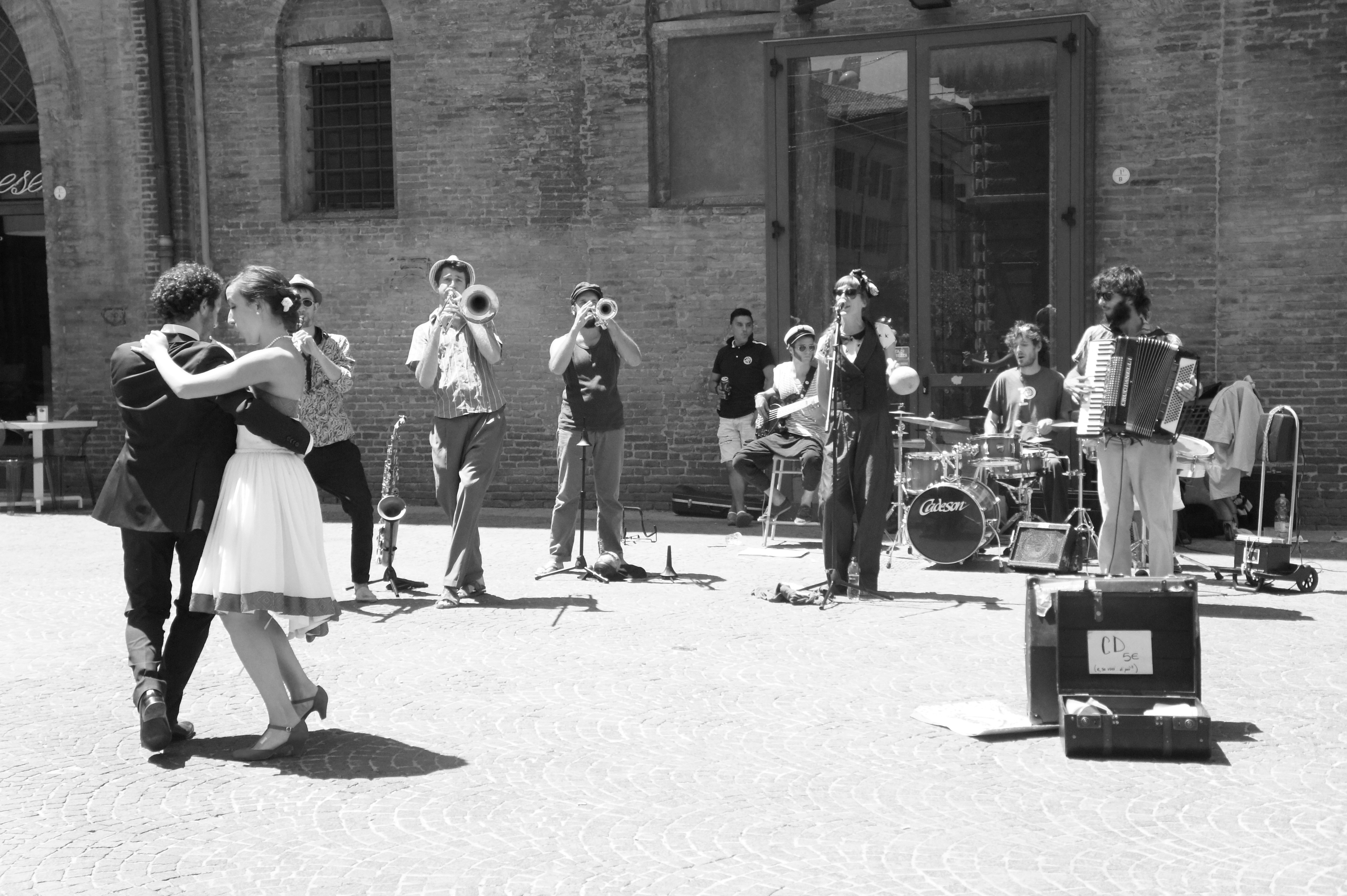 black and white photo of two people dancing in front of band playing in outdoor plaza in front of building