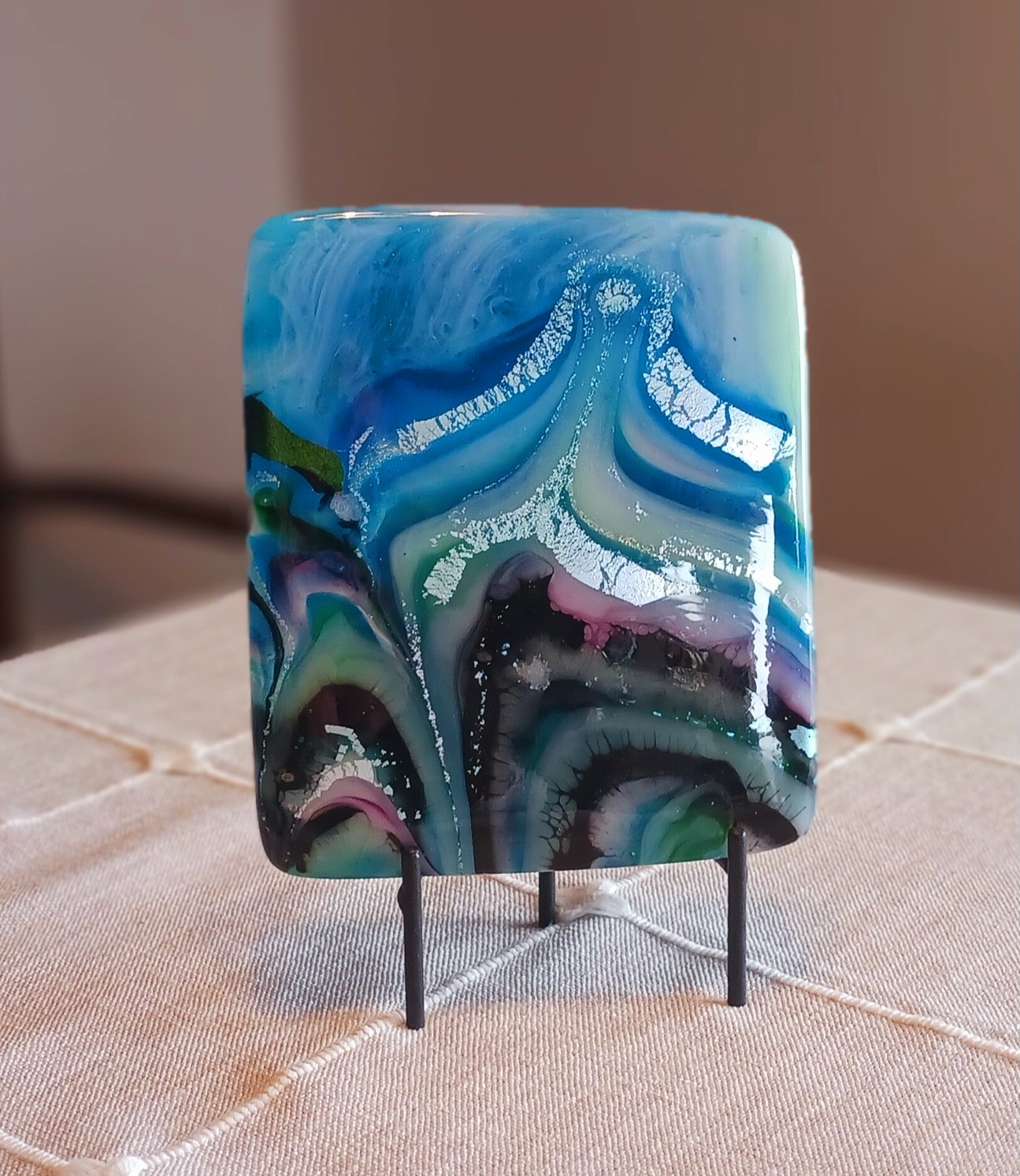 photograph of 3D rectangular piece of glass with swirls of blue, white, violet, green sitting on stand
