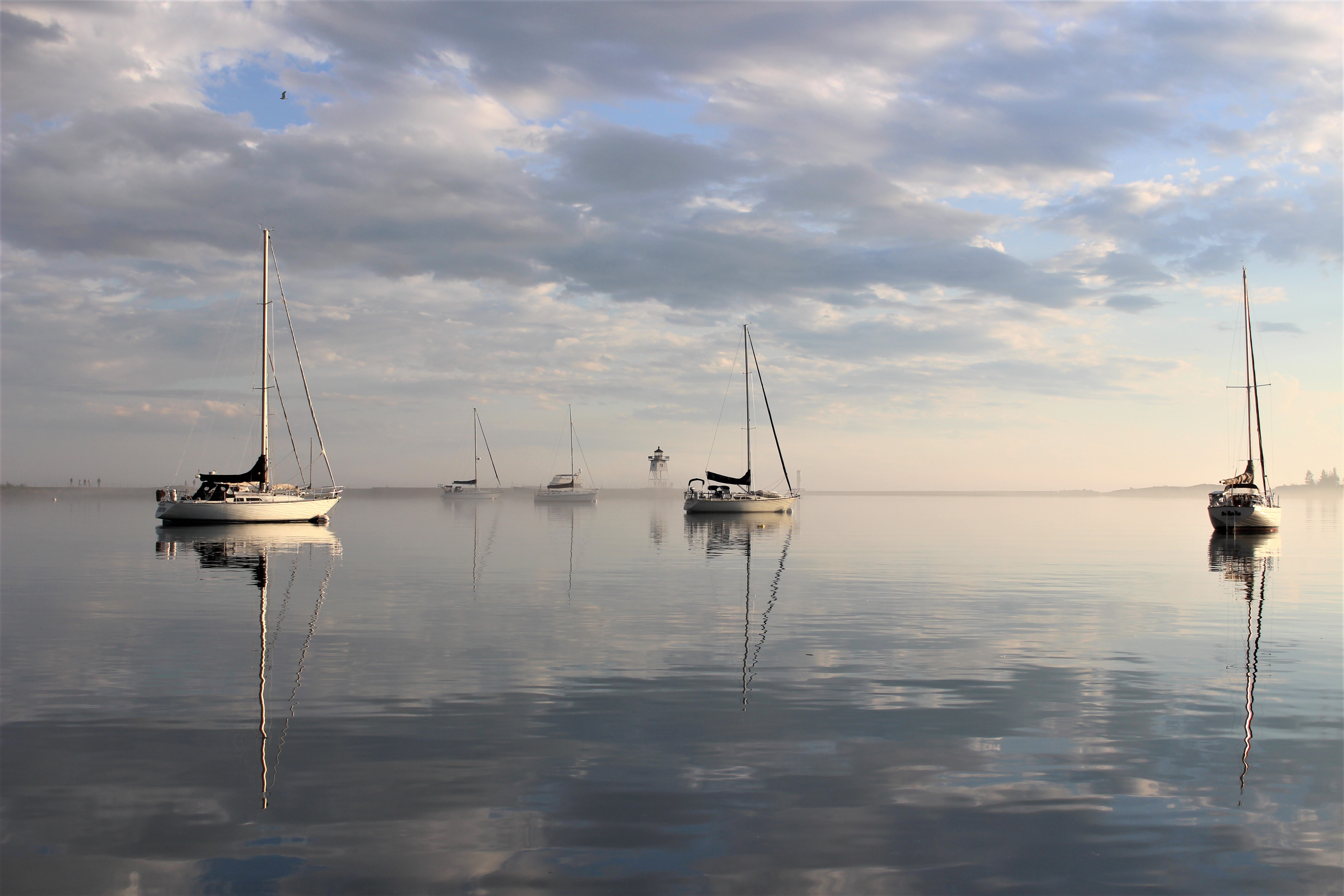color photo of several boats on clear, smooth water with clouds and blue sky all reflected in the surface of the water
