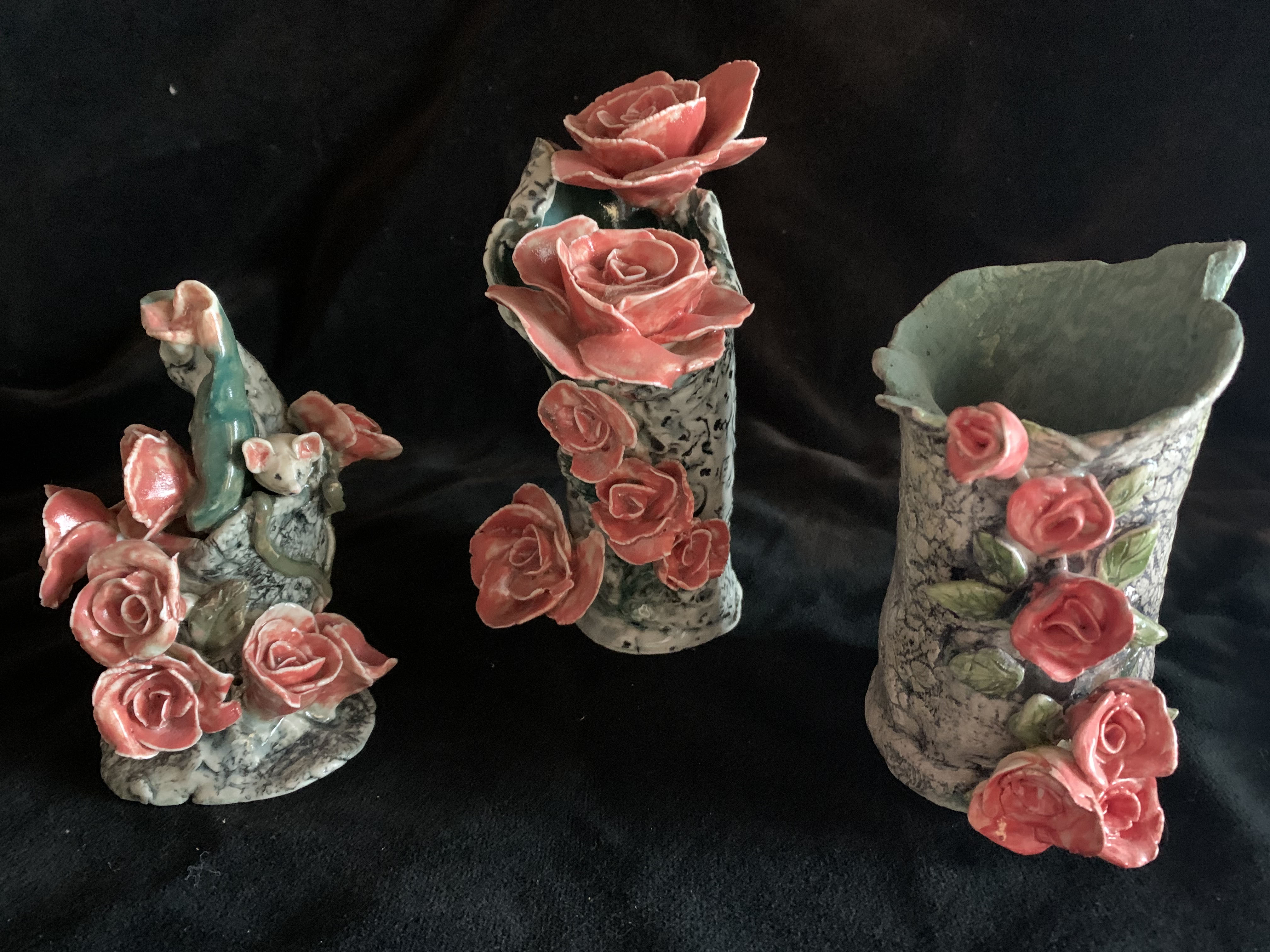 Set of three gray porcelain vessels with pink flowers and a mouse on one of them against a dark background