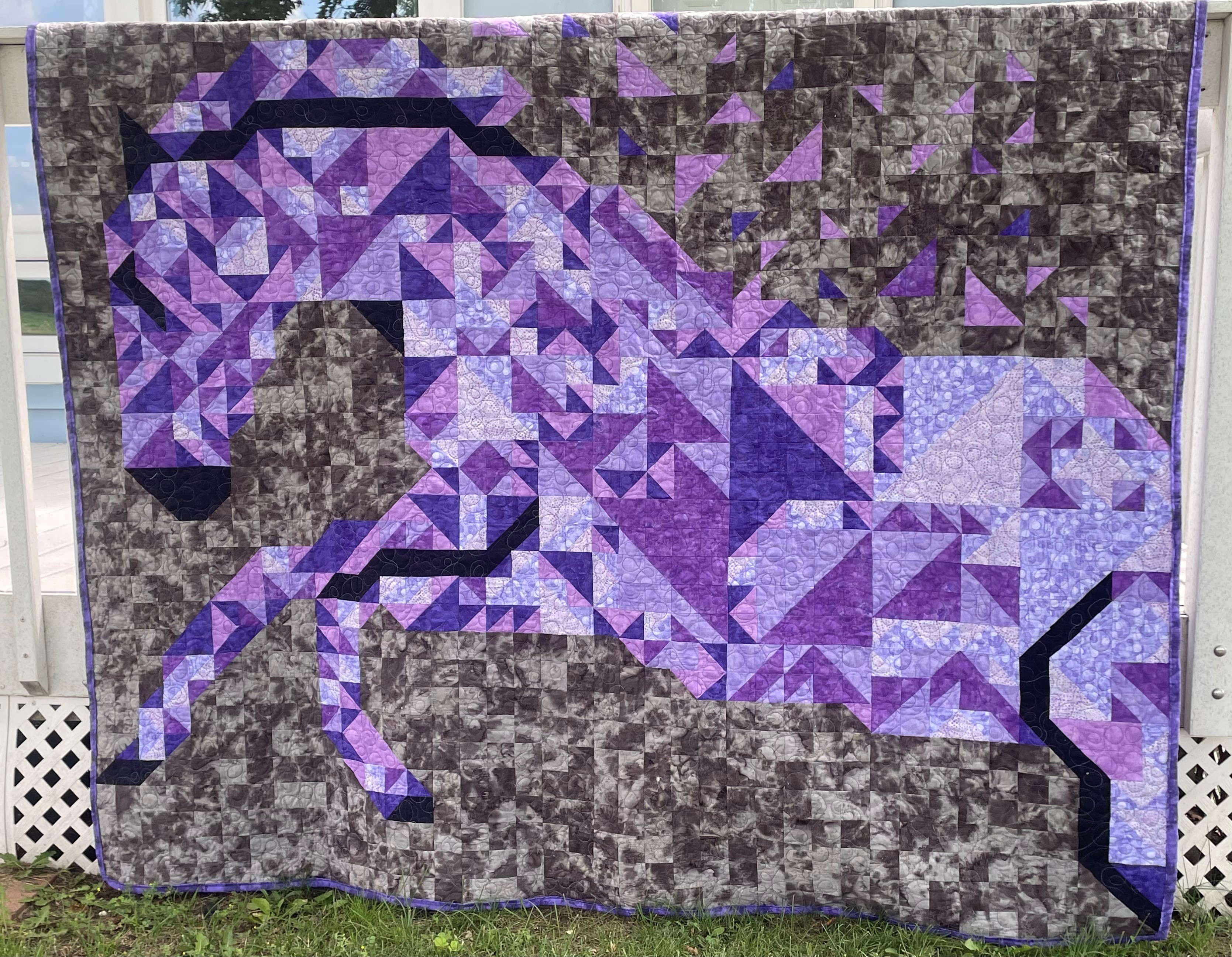 photo of hanging patchwork quilt of a purple horse running with a gray brown background