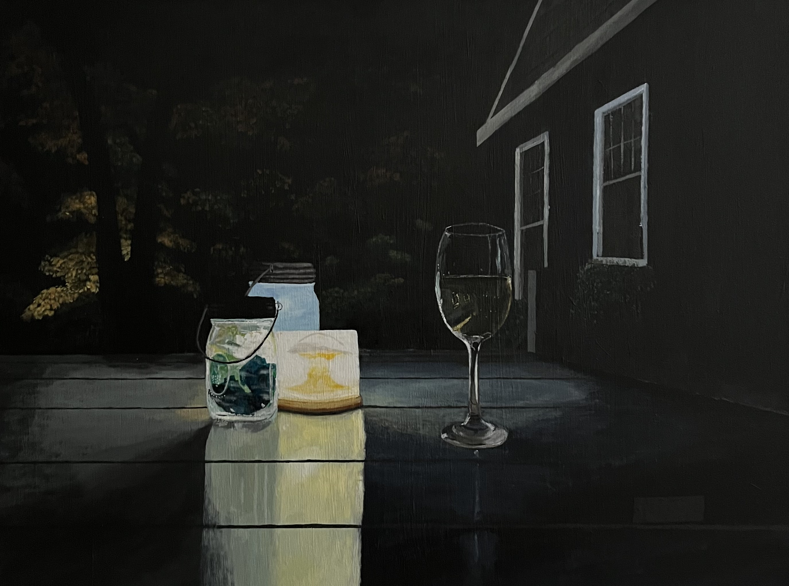 Table outside a house and trees on a dark night with a glass of wine and a couple of jars illuminated by a candle