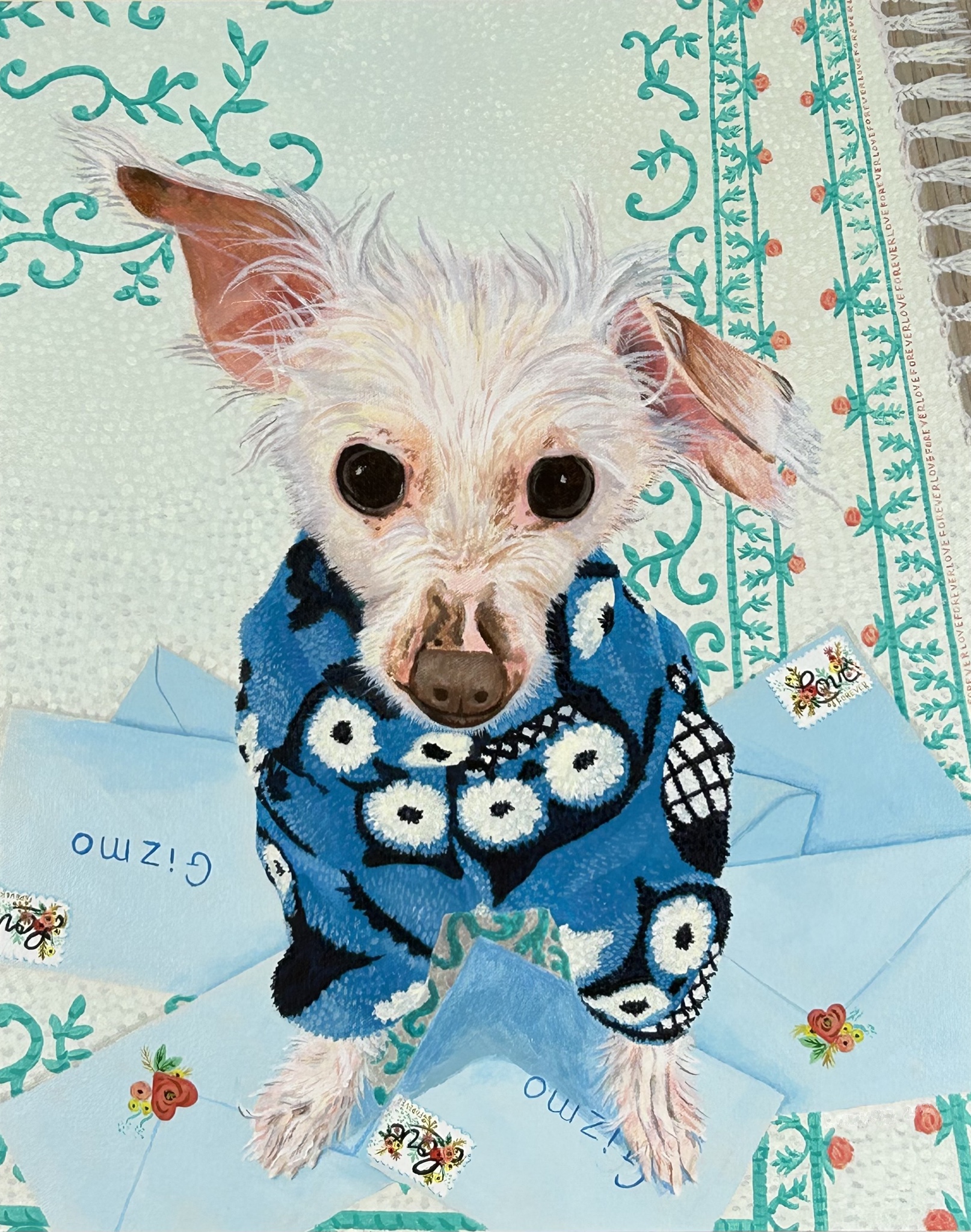 White dog looking up at viewer in blue, white, and black sweater sits on a pile of blue envelopes with the name Gizmo on them, which is sitting on top of a white rug with green leaf and red rose design