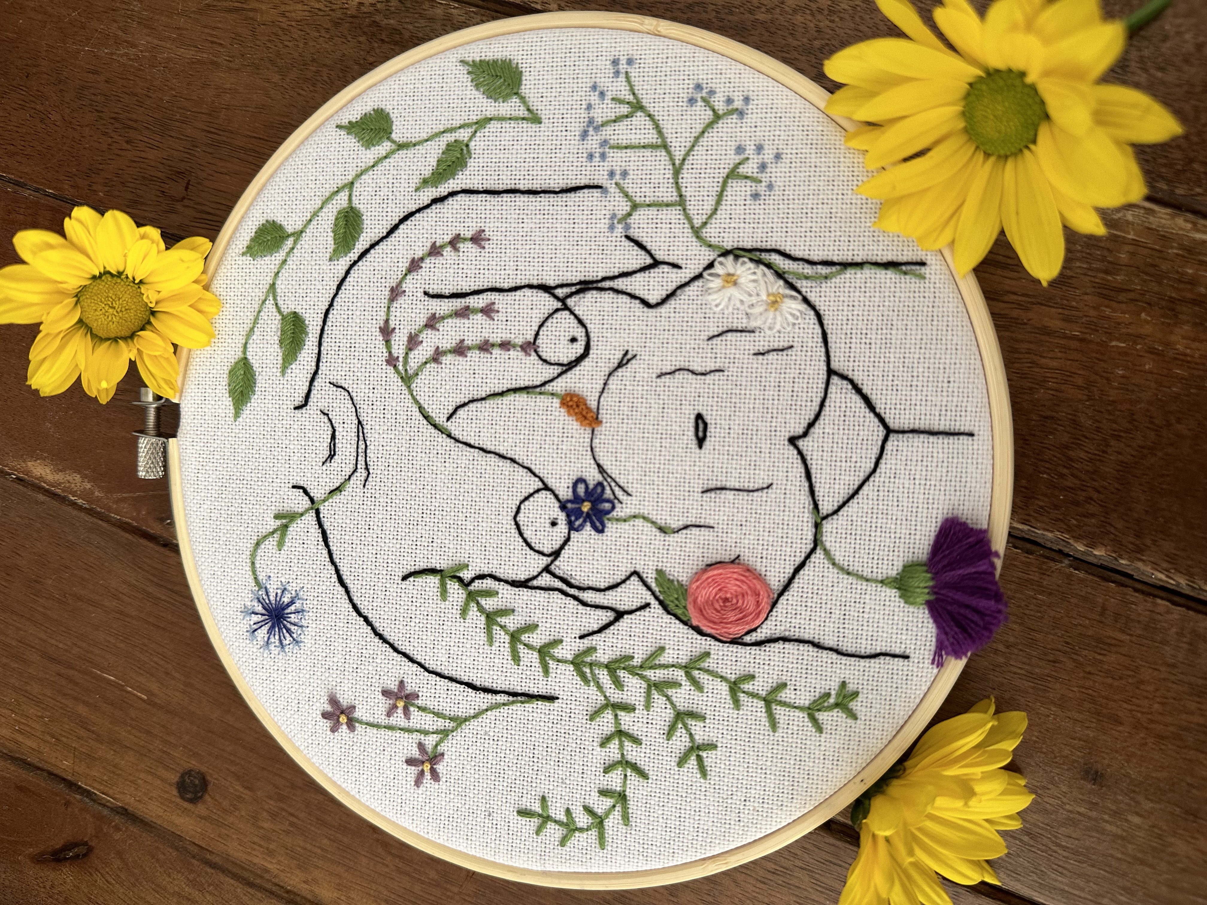 embroidery loop with embroidered naked female body from neck to hips with flowers and leaves around it and yellow flowers around the outside of the loop