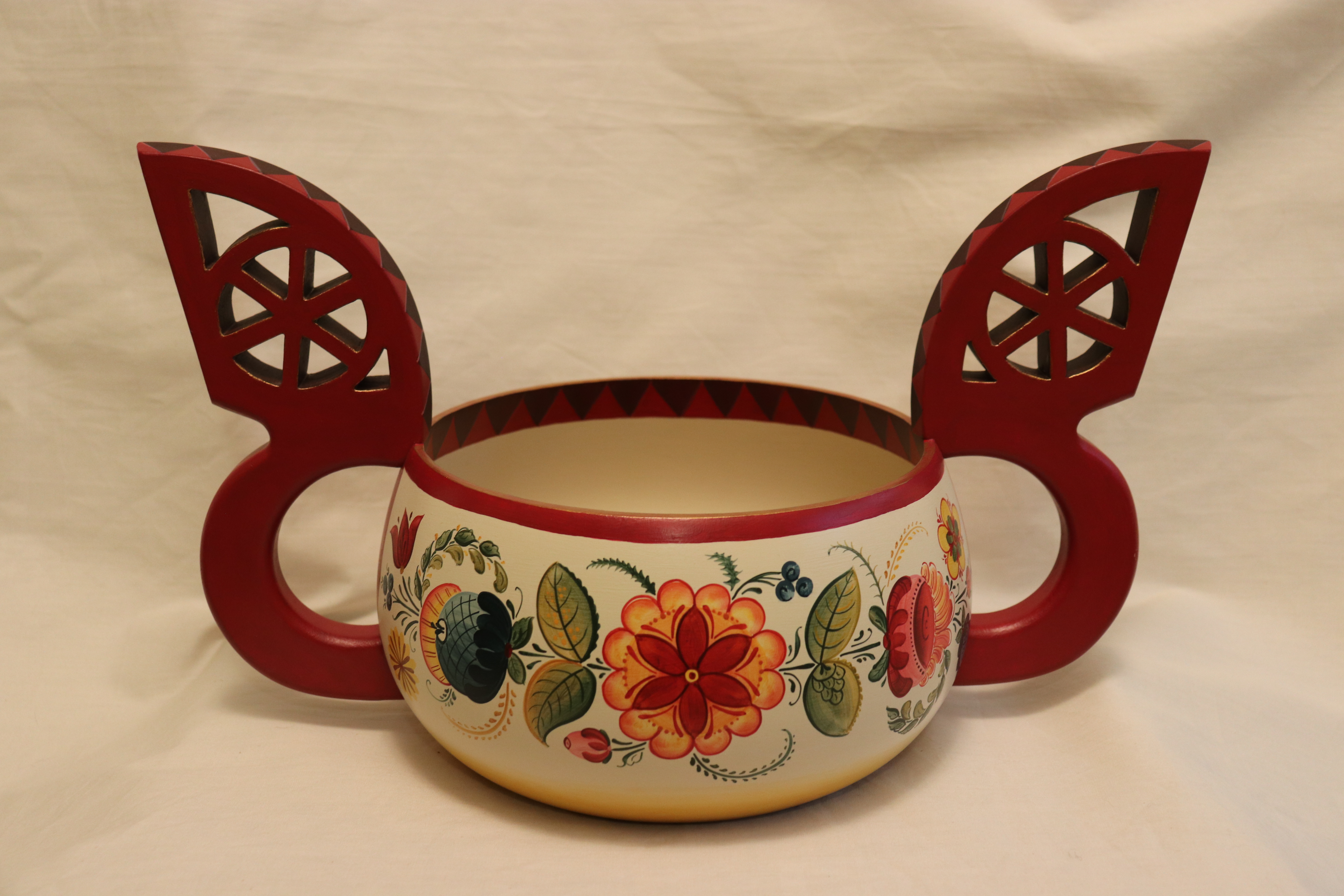 Os style rosemaling of green leaves and orange-red and blue flowers painted with acrylics on a wood ale bowl with red handles and red-brown lip of bowl