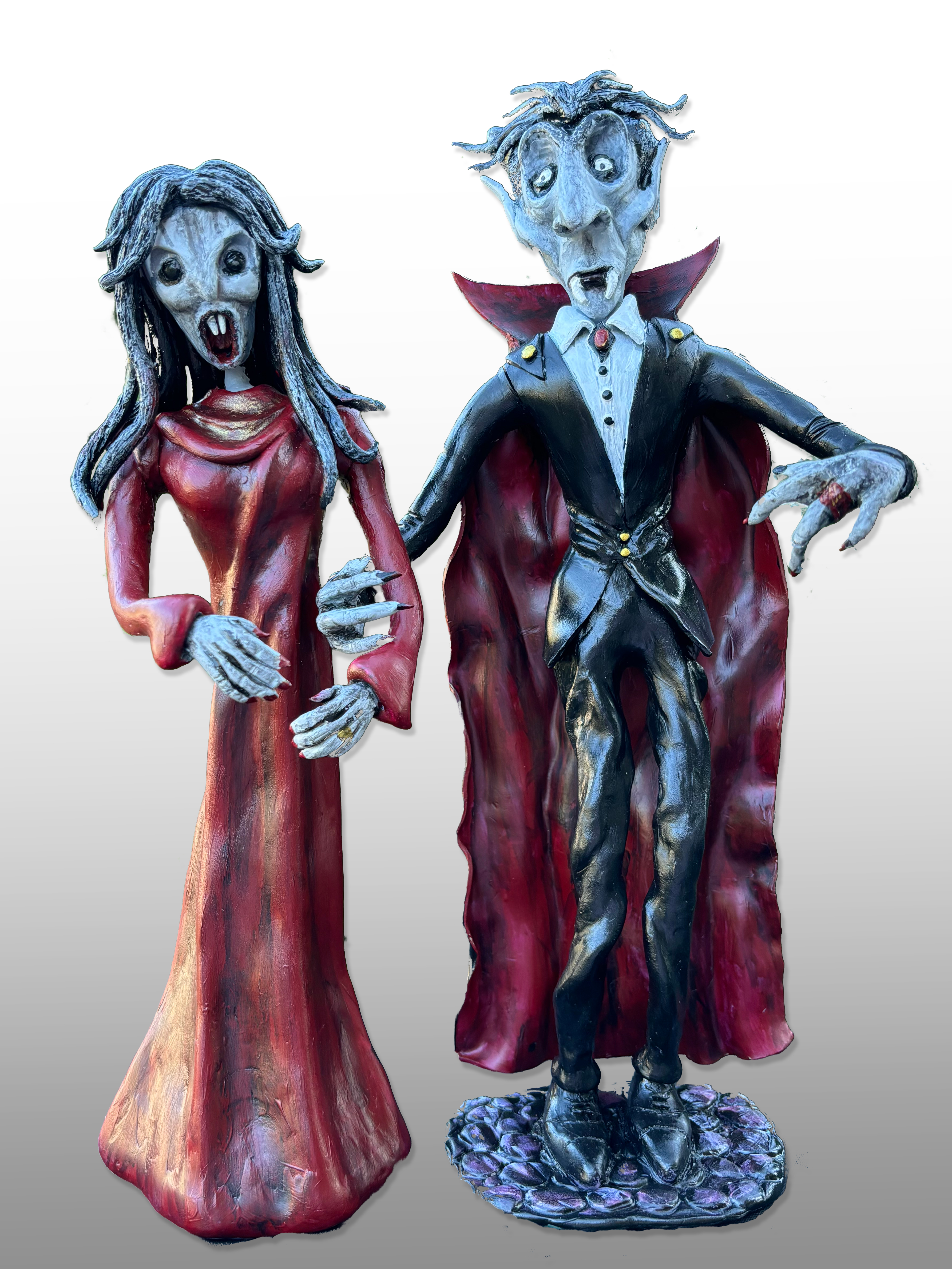 Two clay figurines standing next to each other, one a male vampire in a black suite with a red cloak, the other a female vampire in a long dress with long gray hair