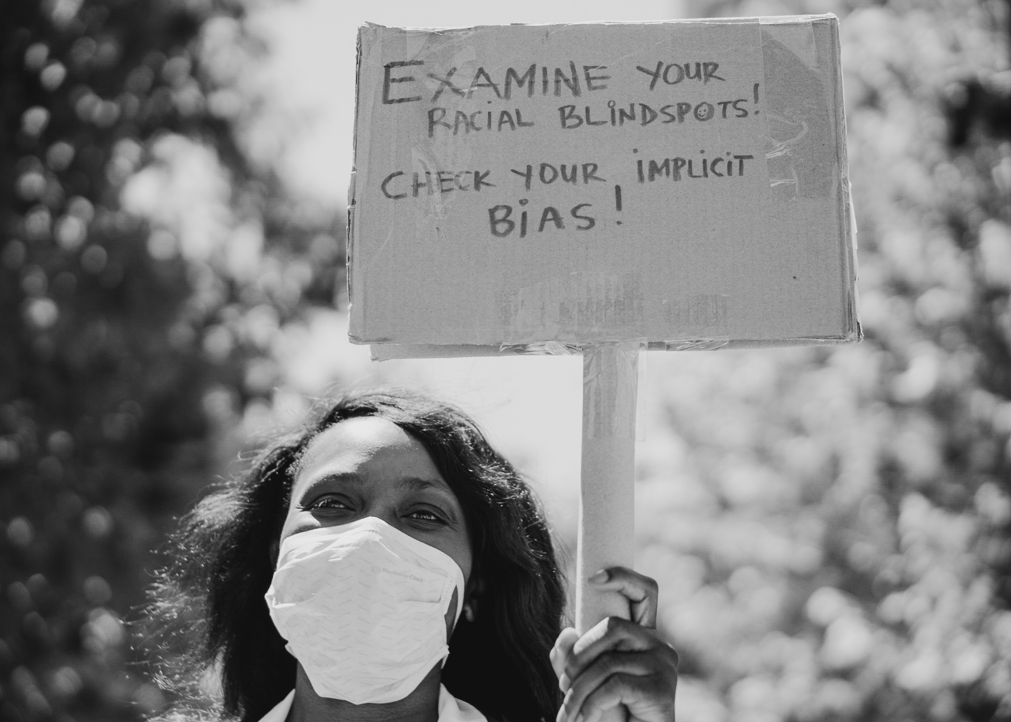 black and white photo of masked person holding sign about bias